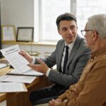 Advogado explicando fator previdenciário para cliente idoso em escritório jurídico, refletindo sobre aposentadoria.